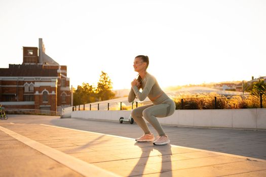 Sporty woman doing jumping squats exercises on stairs in park. Bodyweight training on sunset. Young adult fitness woman exercising outdoor. European woman squats. Athletic caucasian female workout