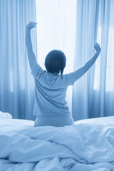 Woman stretching in bed after waking up, back view