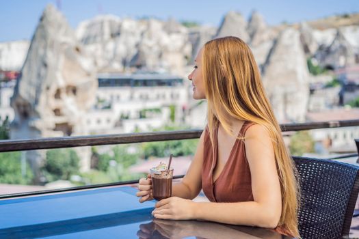 Young woman drinking coffee on the background valley with rock formations and fairy caves near Goreme in Cappadocia Turkey.