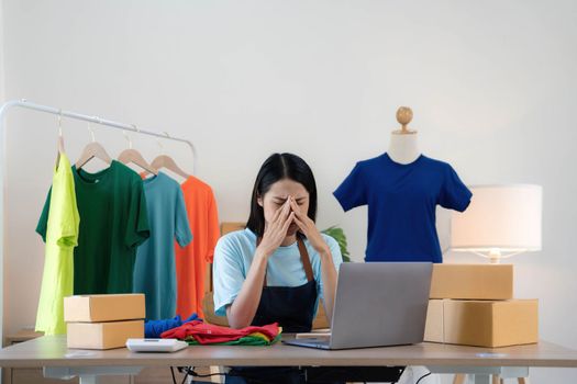 Woman seller SME retail store owner work hard worry stress in bad news on laptop at home office desk. Asian people crisis tailor job issue feel tired tough and upset in cash money loss or loan debt..