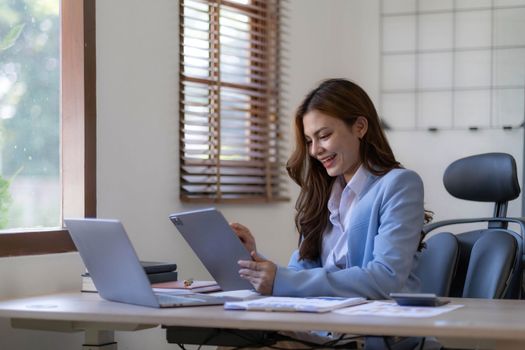 Portrait of smiling business asian woman using smartphone while sitting at workplace...