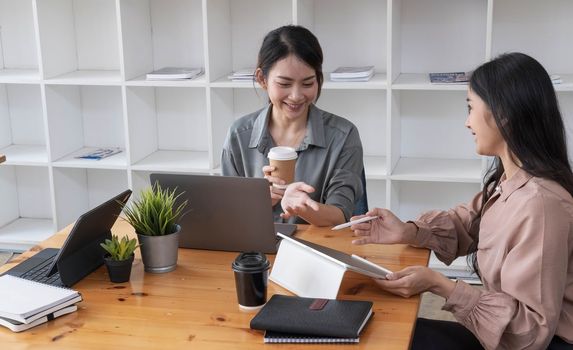 Two young Asian business woman talk, consult, discuss working with new startup project idea presentation analyze plan marketing and investment in the office...