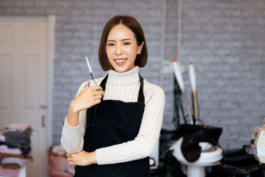 Portrait of a young asian female hairdresser holding qualified haircut tools in her salon for a woman's haircut. Photo job concept for small business owner and haircare.