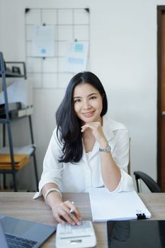 Portrait of a woman business owner showing a happy smiling face as he has successfully invested her business using computers and financial budget documents at work.