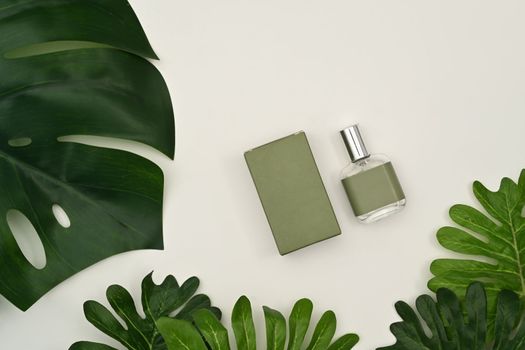Mockup of fragrance perfume bottle with tropical leaves on white background.