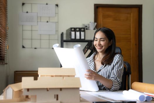 Architecture, building, construction and real estate concept - Happy smiling female architect with blueprint, ruler and living house model on table working at home office. Architect woman