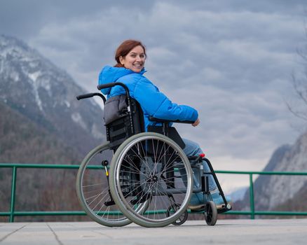 A woman in a wheelchair on a point view admires the high mountains. Thrust to life