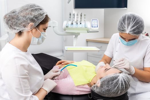 Dentist and assistant performing dental treatment inmodern dental clinic, patient laying in chair