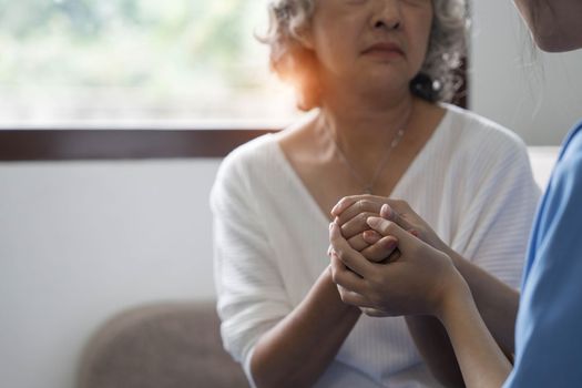 Happy patient is holding caregiver for a hand while spending time together. Elderly woman in nursing home and nurse...