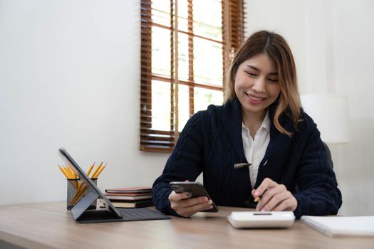 Business asian woman using smartphone for do math finance on wooden desk in office, tax, accounting, financial concept.