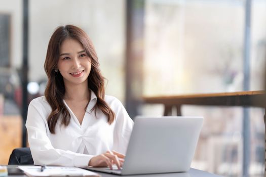 Young woman working on a laptop in the office. Asian businesswoman sitting at her workplace in the office. Beautiful Freelancer Woman working online at her home