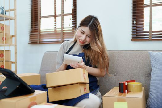 Starting small business entrepreneur of independent Asian woman smiling using computer laptop with cheerful success of online marketing package box items and SME delivery concept.