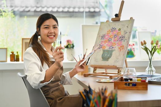 Attractive female artist painting with watercolor on canvas in art workshop. Art, creative hobby and leisure activity concept.