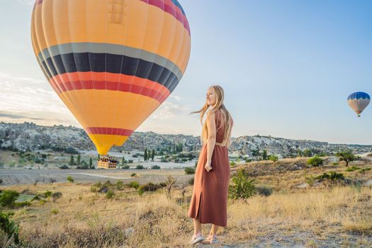 Tourist woman looking at hot air balloons in Cappadocia, Turkey. Happy Travel in Turkey concept. Woman on a mountain top enjoying wonderful view.