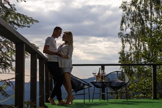 Horizontal sideview shot of a young couple in summer outfit enjoying the mountain view from terrace. Copy space