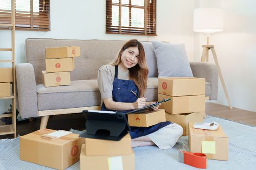 Starting small business entrepreneur of independent young Asian woman online seller is using smart phone and taking orders to pack products for delivery to customers. SME delivery concept.