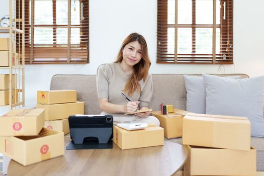 Starting small business entrepreneur of independent young Asian woman online seller is using computer and taking orders to pack products for delivery to customers. SME delivery concept.