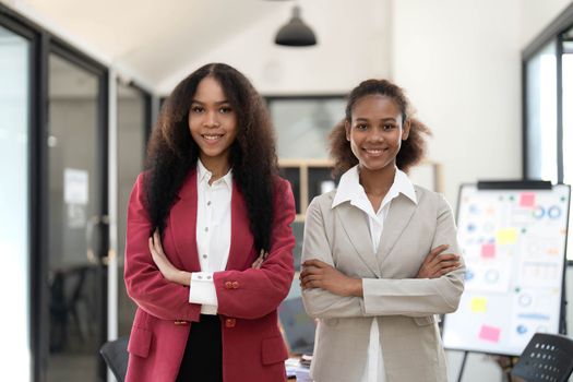 Smiling diverse colleagues businesswomen working on laptop together, looking at screen, stand at desk in office, employees discussing project strategy, sharing ideas.