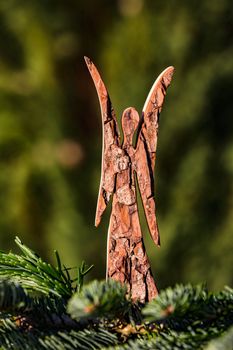 A Christmas angel made of wood isolated behind a pine branch and in front of a natural green background