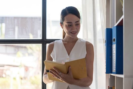 Charming young Asian businesswoman with a smile standing holding documents at the office