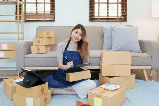 Starting small business entrepreneur of independent young Asian woman online seller is using smart phone and taking orders to pack products for delivery to customers. SME delivery concept.