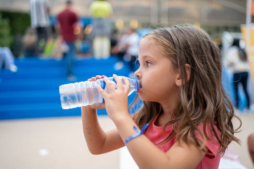 Child drink water from plastic bottle outdoor. Little caucasian girl dressed red shirt drinking pure water after active play game