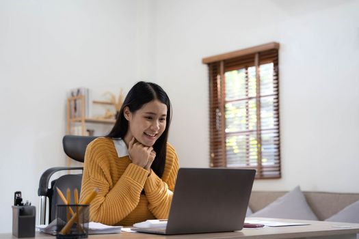 Excited happy woman looking at the laptop computer screen, celebrating an online win, overjoyed young asian female screaming with joy at home.