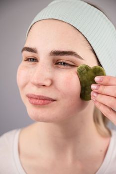 Portrait of a young woman massages her face with a gouache scraper on a white background