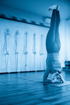 Young yoga woman standing on head in shirshasana. profile view