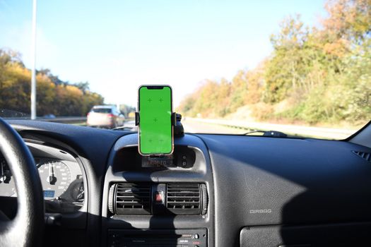 Smartphone with green screen in windshield holder in car interior, road navigation and maps. High quality photo