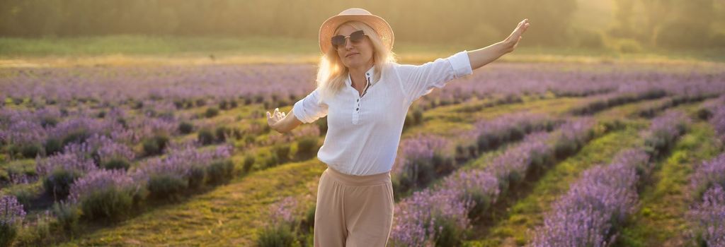 Young woman standing on a lavender field with sunrise on the background.