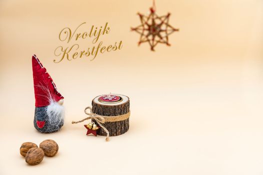 Christmas postcard with text Vrolijk Kerstfeest and a beige background, nuts, wooden candle and a funny gnome