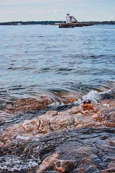 Image of Detail of small waves crashing on rocks in Maine with house on island in background