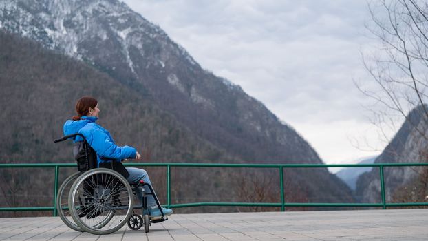 A woman in a wheelchair on a point view admires the high mountains. Thrust to life