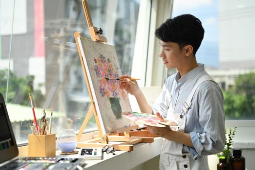 Image of pleased man artist painting picture with watercolor on canvas in art workshop. Art, creative hobby and leisure activity concept.