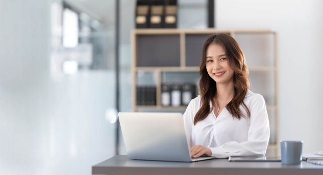 Charming Asian woman working at the office using a laptop Looking at the camera...