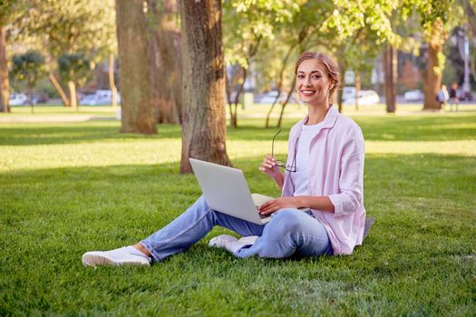Businesswoman sitting grass summer park using laptop Business person working remote. Outdoor Successful european caucasian woman freelancer make video call teacher study work online lessons