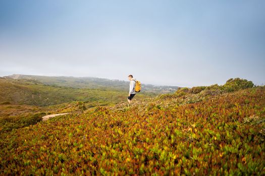 Side view young man with yellow backpack. Man traveler wearing grey hoodie with backpack explore nature. Wanderlust lifestyle. Mountaineering Travel Lifestyle concept.