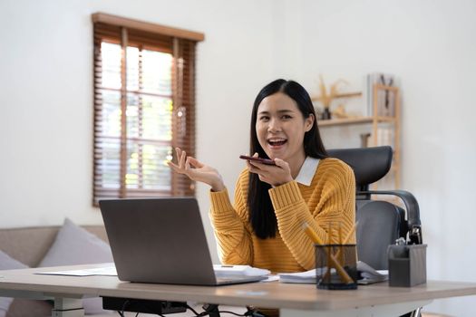 Smiling beautiful Asian businesswoman analyzing chart and graph showing changes on the market and holding smartphone at home.