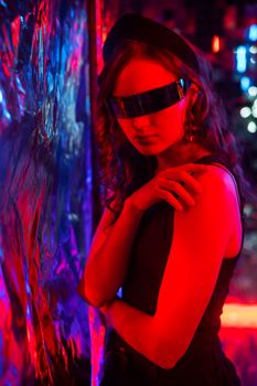 Close-up portrait of caucasian woman in sunglasses in neon light against foil wall