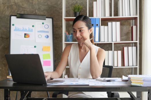 Asian Businesswoman Using laptop computer and working at office with calculator document on desk, doing planning analyzing the financial report, business plan investment, finance analysis concept...