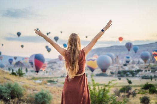 Tourist woman looking at hot air balloons in Cappadocia, Turkey. Happy Travel in Turkey concept. Woman on a mountain top enjoying wonderful view.