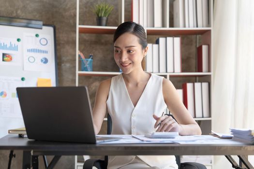 Asian Businesswoman Using laptop computer and working at office with calculator document on desk, doing planning analyzing the financial report, business plan investment, finance analysis concept...