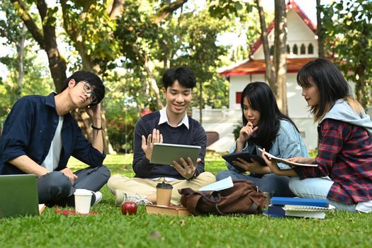 Image of university students doing group project on digital tablet while sitting in university campus. Education, Learning and community.