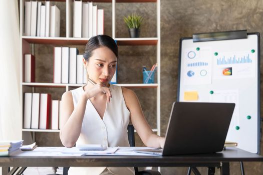 Asian Businesswoman Using laptop computer and working at office with calculator document on desk, doing planning analyzing the financial report, business plan investment, finance analysis concept...