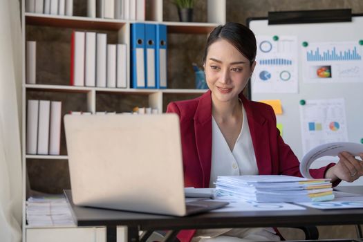 Asian Businesswoman Using laptop computer and working at office with calculator document on desk, doing planning analyzing the financial report, business plan investment, finance analysis concept...