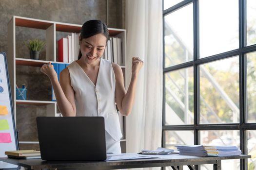 Pretty Asian businesswoman sitting on a laptop And the work came out successfully and the goal was achieved, happy and satisfied with her...