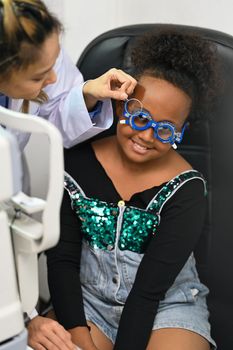 Smiling girl checking eye vision with ophthalmologist for spectacles glasses. Eye health check, ophthalmology concept.