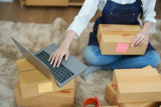 Starting small business entrepreneur of independent Asian woman smiling using computer laptop with cheerful success of online marketing package box items and SME delivery concept.