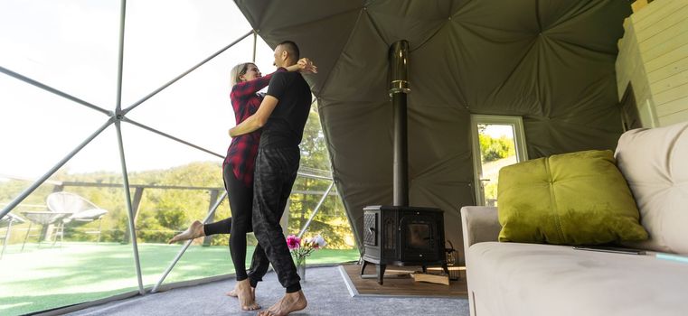 couple looking at nature from geo dome tents. Green, blue, orange background. Cozy, camping, glamping, holiday, vacation lifestyle concept. Scenic outdoors cabin.